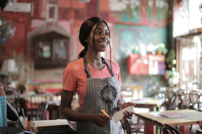 A cheerful waitress with a notepad takes orders inside a vibrant restaurant.